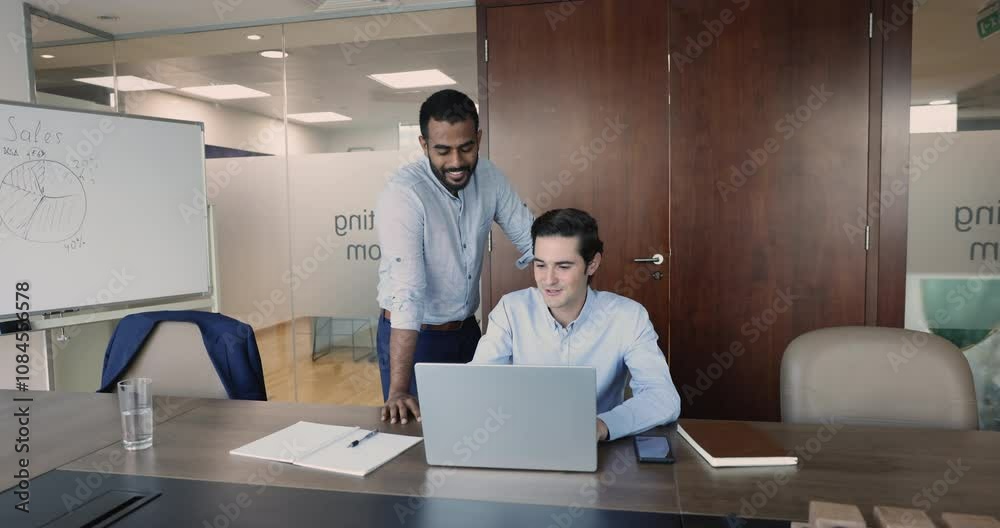 Two multiethnic male business partners talking at laptop, discussing online project, web content, application for job, startup presentation, looking, pointing at monitor, enjoying teamwork