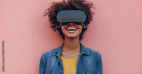 Young woman enjoys virtual reality experience while smiling against a pink ba...