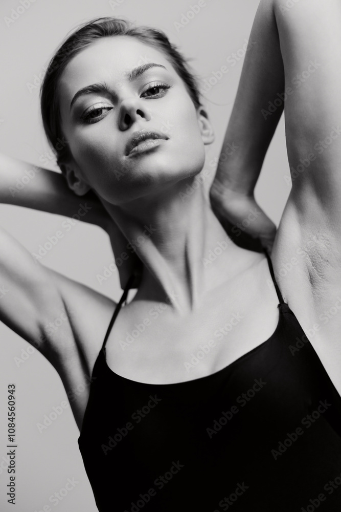 Elegant young woman posing confidently in a black outfit, with her arms raised, showcasing a graceful silhouette against a soft gray background. Elegant young woman posing confidently in a black outfit, with her arms raised, showcasing a graceful silhouette against a soft gray background.