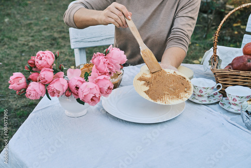 Woman spreading delicious hazelnut cream on a waffle at an outdoor picnic.  Pink peonies and teacups add a touch of elegance to the scene. Perfect for autumnal themes and food blogs. photo