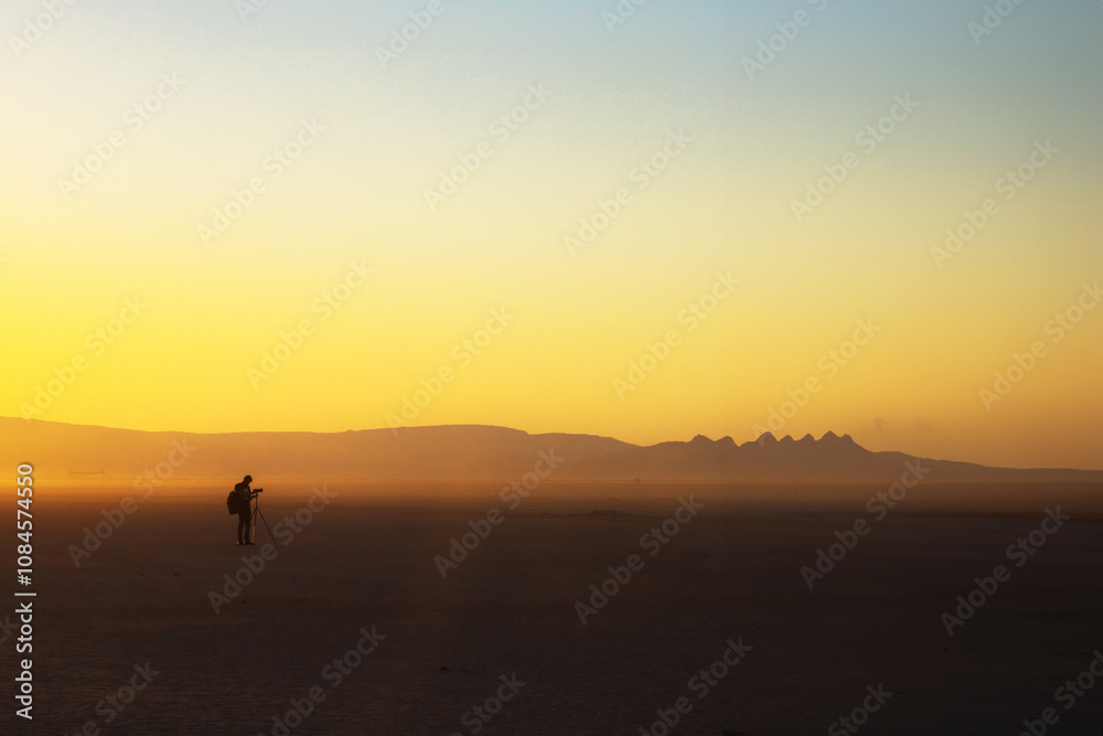 Fototapeta premium At sunrise and sunset in the vast expanse of Wadi Rum, people engage in various activities, surrounded by the enchanting beauty of the desert. The golden hour casts a warm glow over the hazy landscape