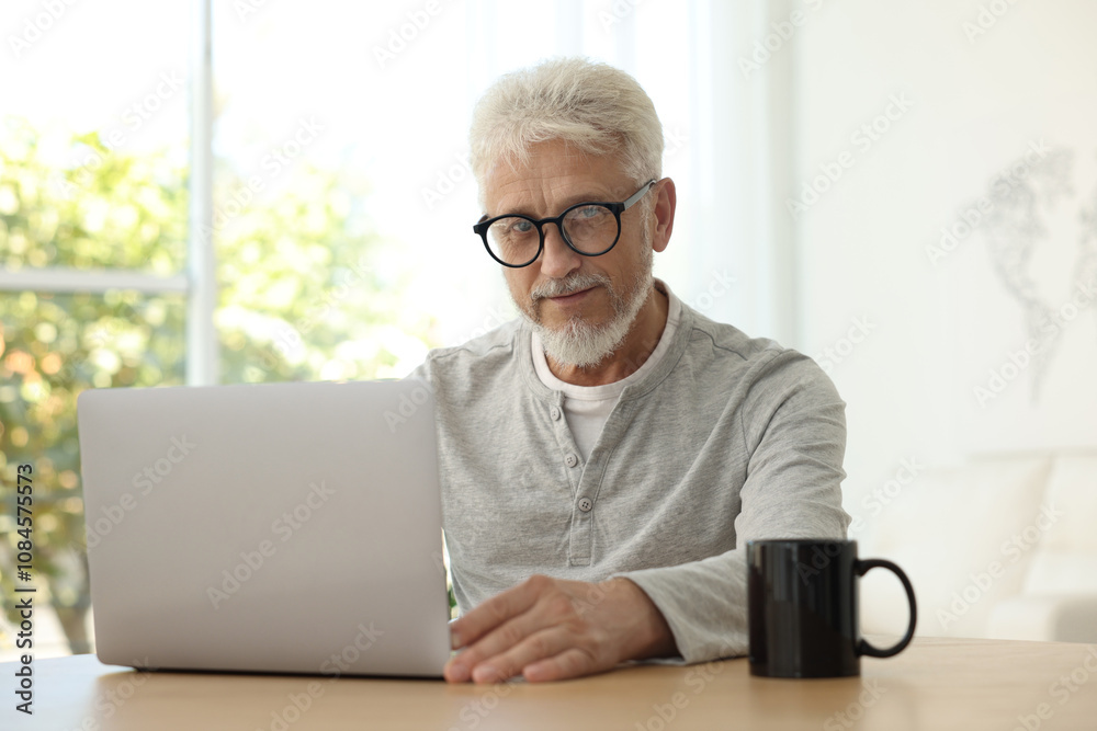 Senior man using laptop at table indoors Senior man using laptop at table indoors