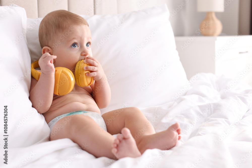 Cute little baby with headphones on bed at home, space for text Cute little baby with headphones on bed at home, space for text