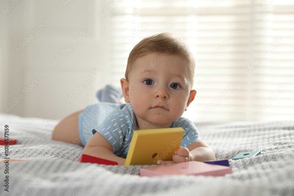 Cute little baby with toys on bed at home