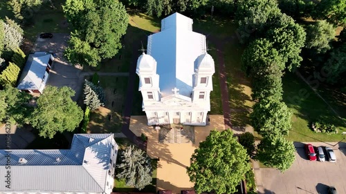 Areal reveal of the Church in Jonava, Lithuania, surrounded by green trees, Neris river, and a charming townscape.