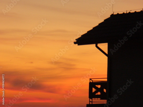 Orange red sky at sunset and fragment of dark wall of house with roof and balcony. Topics: apartment, house, construction, weather, atmosphere, beauty of nature, dusk, evening