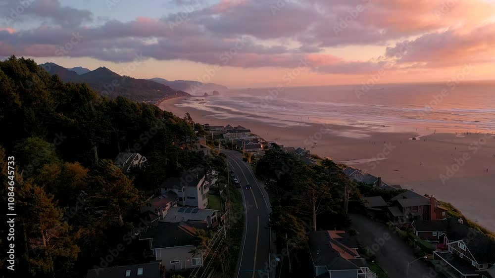 Aerial drone footage of cars driving through a beach town located right next to the ocean. Cannon Beach and haystack rock in Oregon during golden hour at sunset.