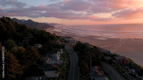 Aerial drone footage of cars driving through a beach town located right next to the ocean. Cannon Beach and haystack rock in Oregon during golden hour at sunset.