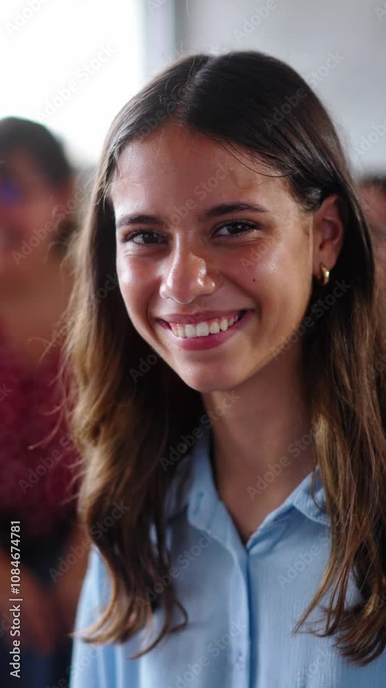 Vertical. Primary school girl poses looking smiling at camera sitting in class with classmates in background. Group children gathered in study room. Portrait happy Caucasian elementary female student Vertical. Primary school girl poses looking smiling at camera sitting in class with classmates in background. Group children gathered in study room. Portrait happy Caucasian elementary female student