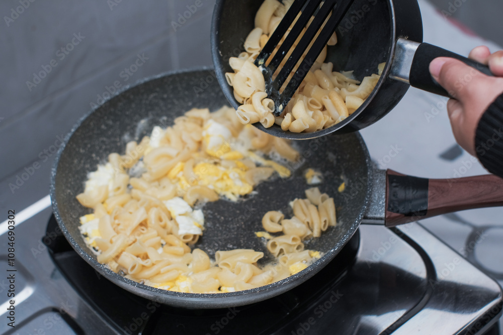 A closeup of a women hand cooking the pasta macaroni or penne pasta in wok pan, pouring the pasta macaroni or penne pasta to pan, cooking pasta homemade. A closeup of a women hand cooking the pasta macaroni or penne pasta in wok pan, pouring the pasta macaroni or penne pasta to pan, cooking pasta homemade.