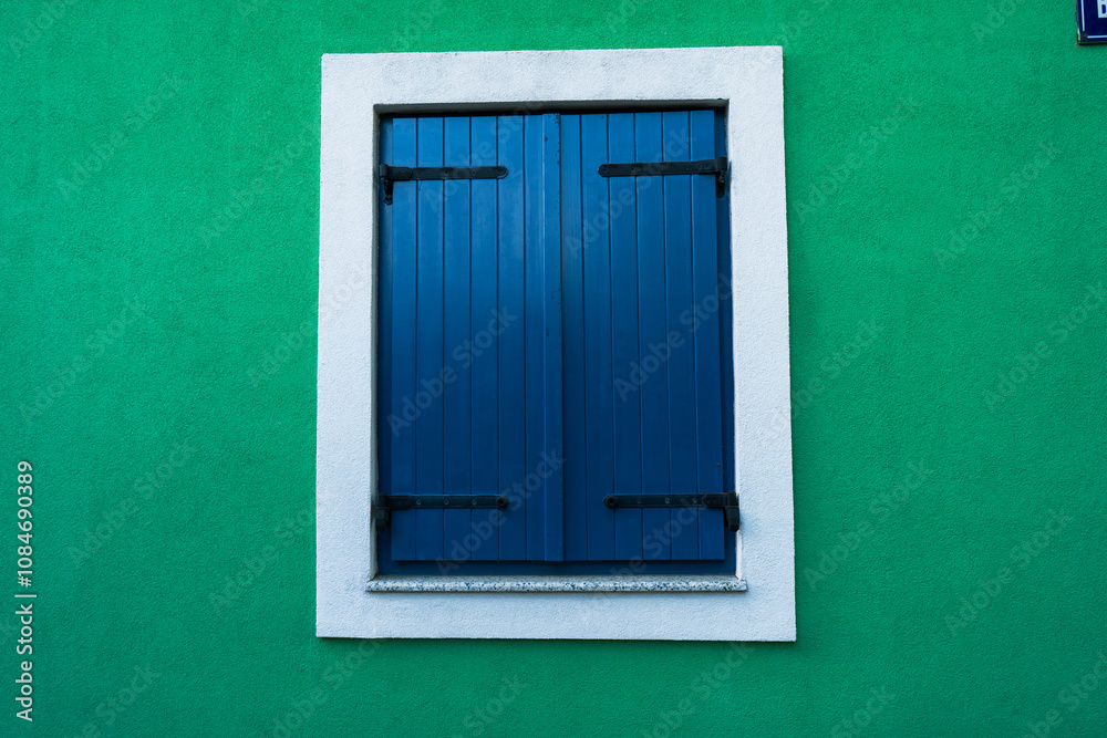 Fototapeta premium Blue window shutters on green wall - background wallpaper