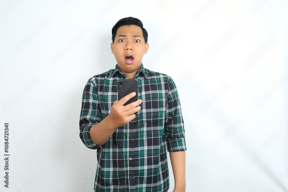 shocked asian man holding smartphone isolated on white background, wear casual shirt, looking at camera shocked asian man holding smartphone isolated on white background, wear casual shirt, looking at camera
