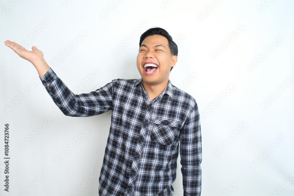 carefree asian man presenting hand with laughing expression showing joy and playful emotion wearing casual plaid shirt isolated on white background carefree asian man presenting hand with laughing expression showing joy and playful emotion wearing casual plaid shirt isolated on white background