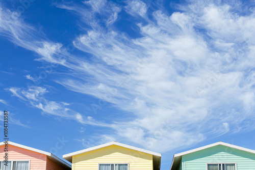 row of beach houses in mint, coral, yellow and blue, cirrus clouds in azure sky