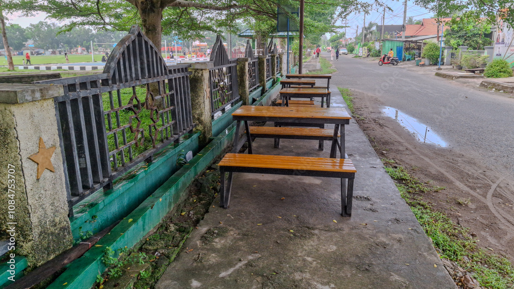 A serene park scene featuring wooden picnic tables under lush green trees, perfect for outdoor relaxation and gatherings A serene park scene featuring wooden picnic tables under lush green trees, perfect for outdoor relaxation and gatherings