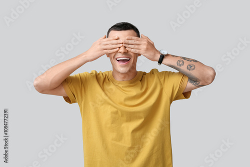 Portrait of happy young man covering eyes while laughing on grey background