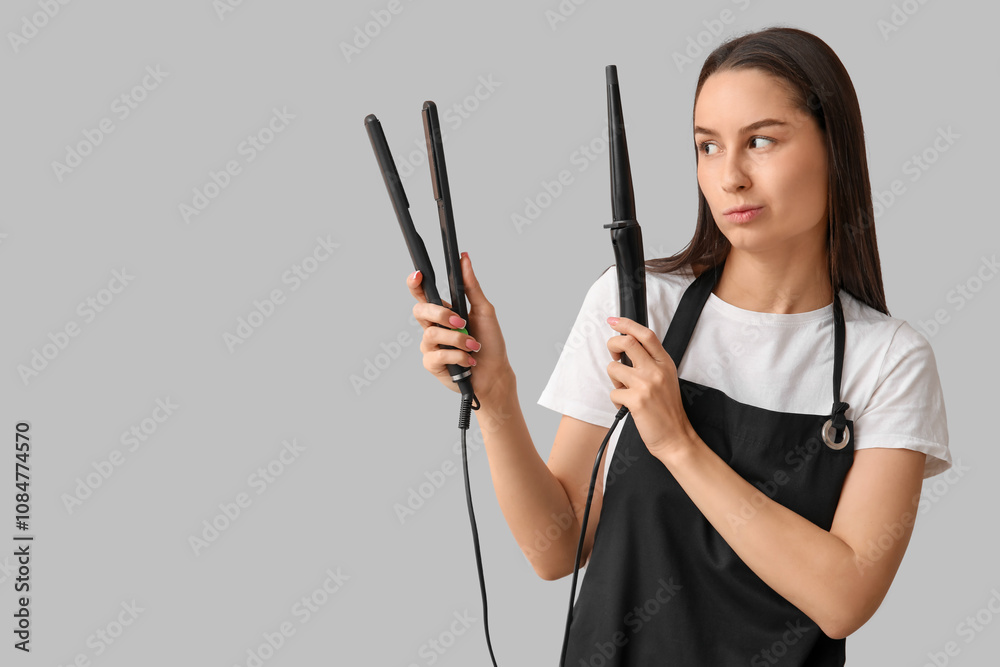 Female hairdresser with curling iron and flattening iron on grey background Female hairdresser with curling iron and flattening iron on grey background