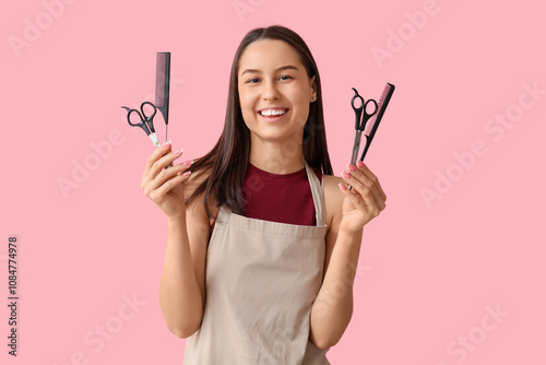 Female hairdresser with scissors and combs on pink background