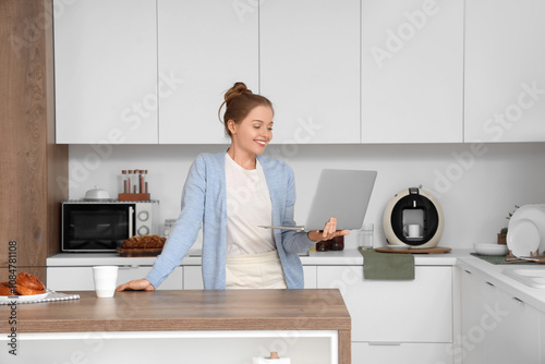 Young woman with modern laptop in kitchen