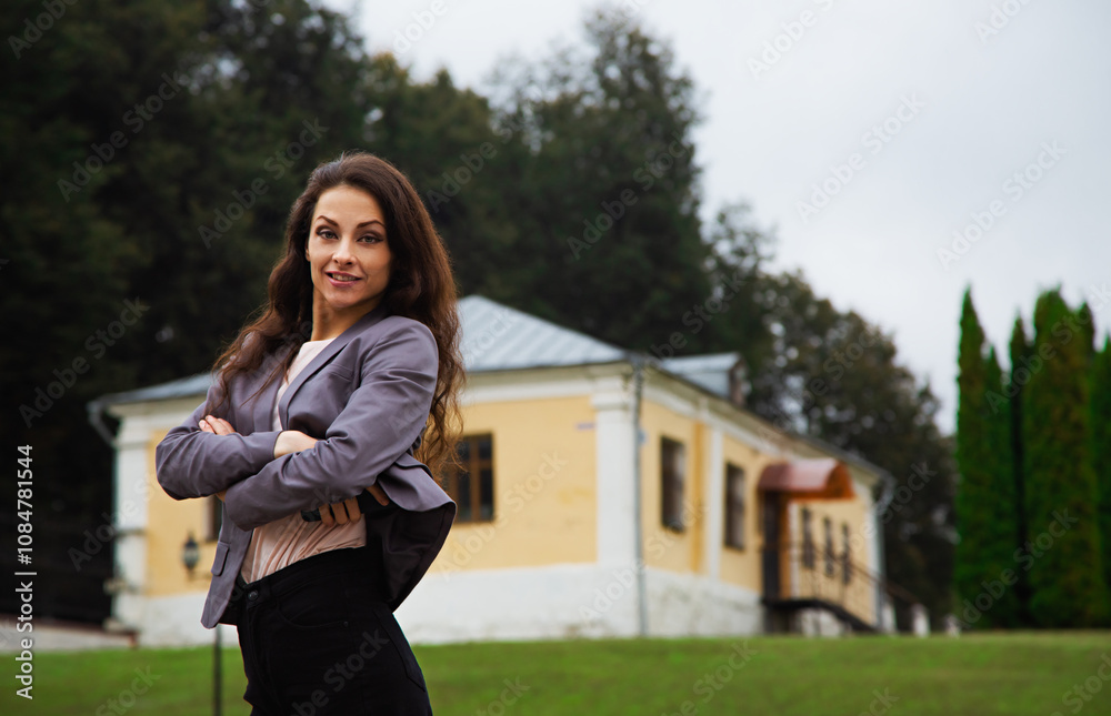 Beautiful happy toothy smiling business woman with long brown hair in grey suit standing outdoor nature street summer green background near the office building. Beautiful happy toothy smiling business woman with long brown hair in grey suit standing outdoor nature street summer green background near the office building.