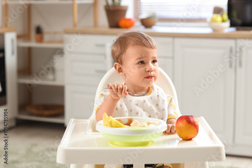 Cute little baby eating tasty fruits and sitting on chair in kitchen at home