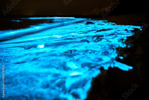 A captivating close-up of bioluminescent waves illuminating the shoreline in a serene glow, creating a magical nighttime scene.