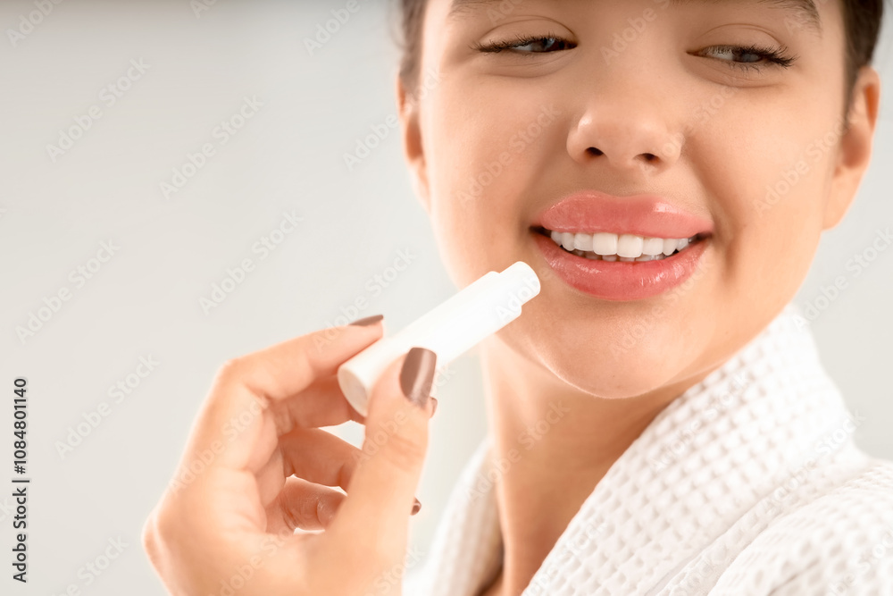 Beautiful young woman applying lip balm on light background, closeup Beautiful young woman applying lip balm on light background, closeup