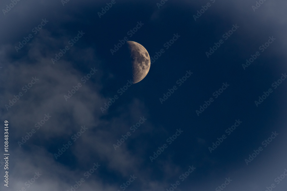 The moon in the dark blue sky with white clouds, closeup