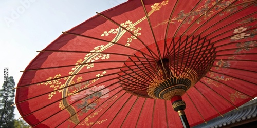 Traditional Red and Gold Parasol A beautifully painted red parasol showcasing a coiled s its intricate patterns embellished with golden accents adding a touch of grandeur. photo