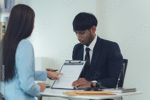 Business Contract Review: Focused discussion between a male and female professional reviewing paperwork during a business meeting. A serious and attentive atmosphere is depicted. 