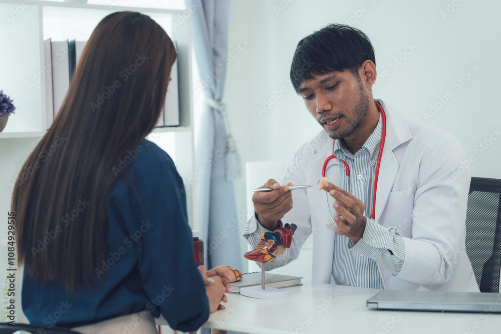 Fototapeta premium Doctor Explaining Medical Model: A doctor uses a model to explain a medical condition to a patient. The scene is set in a professional medical office, demonstrating a doctor-patient interaction. 