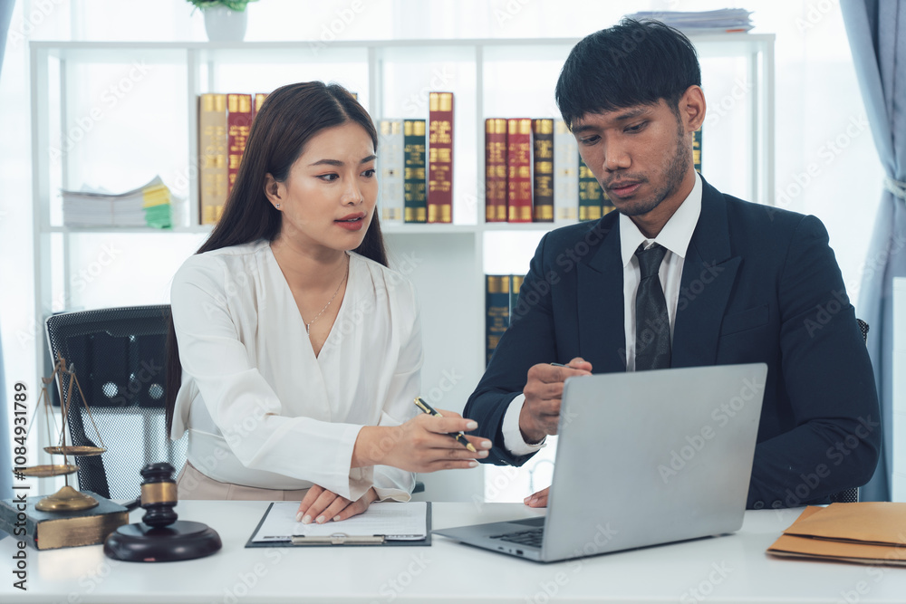Legal Professionals Collaborating: Two focused lawyers, a man and a woman, work together on a laptop in a modern office setting. Legal Professionals Collaborating: Two focused lawyers, a man and a woman, work together on a laptop in a modern office setting.