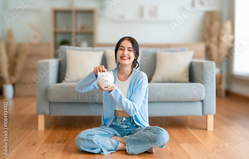 Young Asian woman holding piggy bank and sitting on the floor at home. Save money and financial investment photo