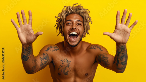 Positive, tattooed Hispanic or Latino man with funky curly hair showing both his hands in a gesture of fun and optimism embodying a hakuna matata attitude with zest for life on a yellow background