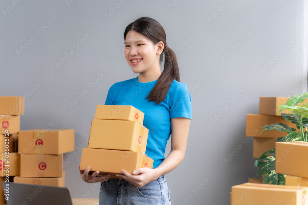 Young Entrepreneur's Success: A smiling woman, surrounded by boxes, holds up a stack of packages, symbolizing the growth and fulfillment of her online business.  