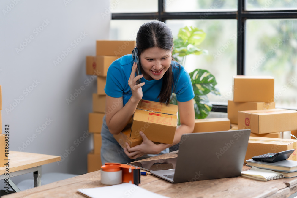 Busy Entrepreneur: A smiling woman manages her e-commerce business, multitasking with a phone call, laptop, and boxes. She's surrounded by packages. Busy Entrepreneur: A smiling woman manages her e-commerce business, multitasking with a phone call, laptop, and boxes. She's surrounded by packages.