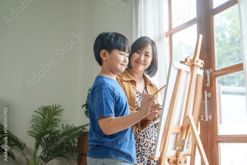 A mother teaches her young son art at home, smiling warmly as they enjoy painting together using an easel, creating colorful memories and strengthening their bond in a creative environment