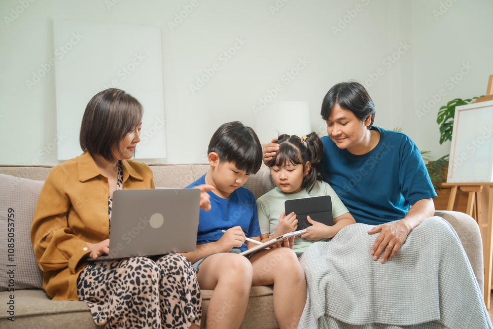 Asian parents and children sit together on a sofa at home, laughing and enjoying family time while using various devices like laptops, phones, and tablets, showcasing a tech-savvy lifestyle Asian parents and children sit together on a sofa at home, laughing and enjoying family time while using various devices like laptops, phones, and tablets, showcasing a tech-savvy lifestyle