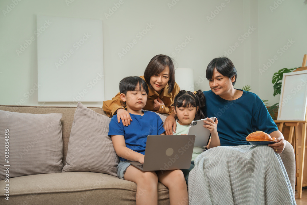 Asian parents and children sit together on a sofa at home, laughing and enjoying family time while using various devices like laptops, phones, and tablets, showcasing a tech-savvy lifestyle Asian parents and children sit together on a sofa at home, laughing and enjoying family time while using various devices like laptops, phones, and tablets, showcasing a tech-savvy lifestyle