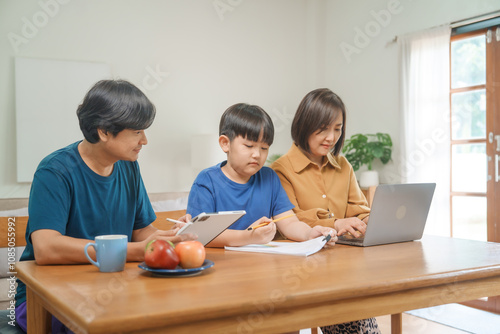 Asian parents and their children sit together at the table in the morning, studying online using tablets and computers, fostering a productive and focused family learning environment