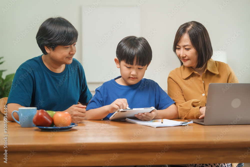 Asian parents and their children sit together at the table in the morning, studying online using tablets and computers, fostering a productive and focused family learning environment Asian parents and their children sit together at the table in the morning, studying online using tablets and computers, fostering a productive and focused family learning environment