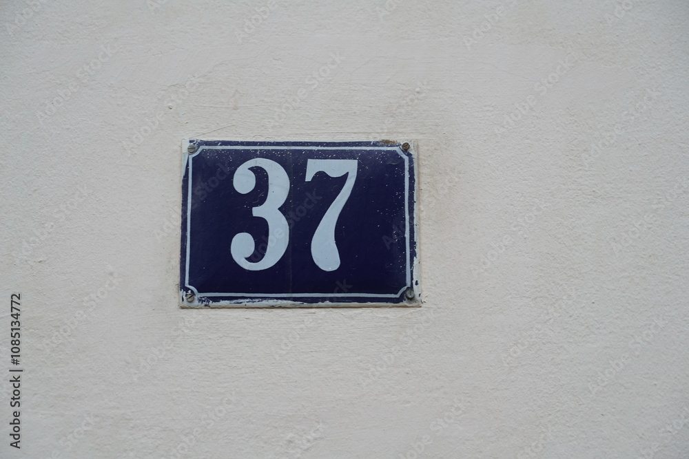 White Number 37 on Blue Plate Isolated Against Wall Background White Number 37 on Blue Plate Isolated Against Wall Background