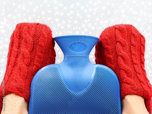 Photography Blue hot water bottle and two feet with red bed socks in front of a snow background