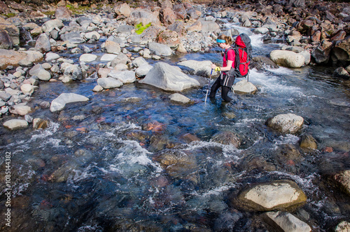 young woman crossing rocky stream during wilderness hike photo