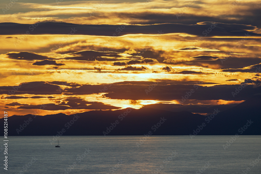 Fototapeta premium This image captures a breathtaking sunset over Aegean sea in Greece, with dramatic clouds casting intricate shadows and colours, conveying a sense of tranquillity and awe.