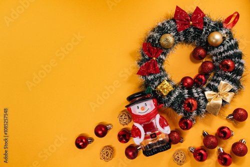 Festive arrangement with a snowman figurine, holiday wreath, and decorations, perfect for Christmas-themed projects on a vibrant orange backdrop.