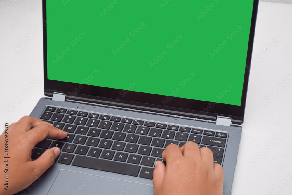 Hands typing on a laptop keyboard, a blank green screen displaying Hands typing on a laptop keyboard, a blank green screen displaying