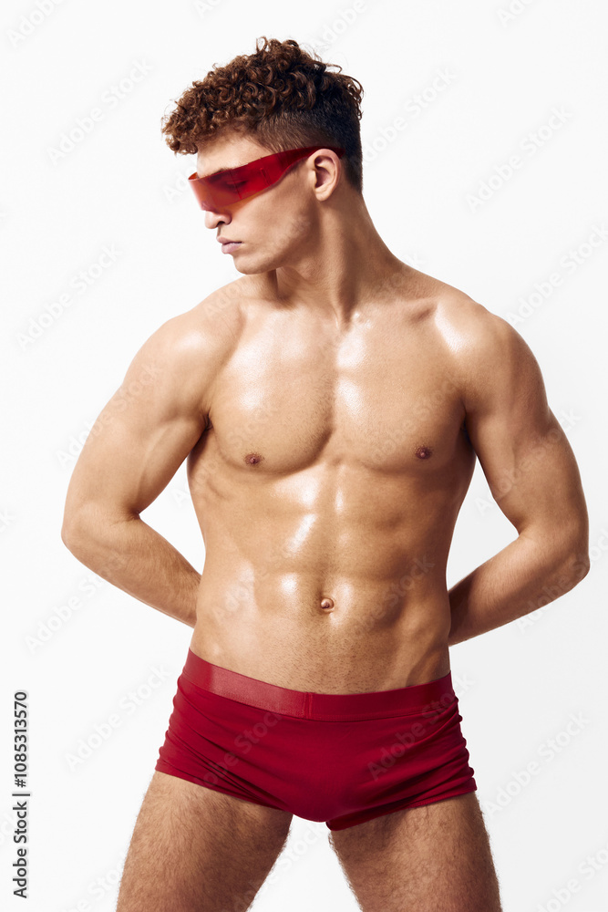 Confident young male model posing in stylish red swimwear, showcasing toned physique and wearing trendy sunglasses. Fashion and fitness concept.