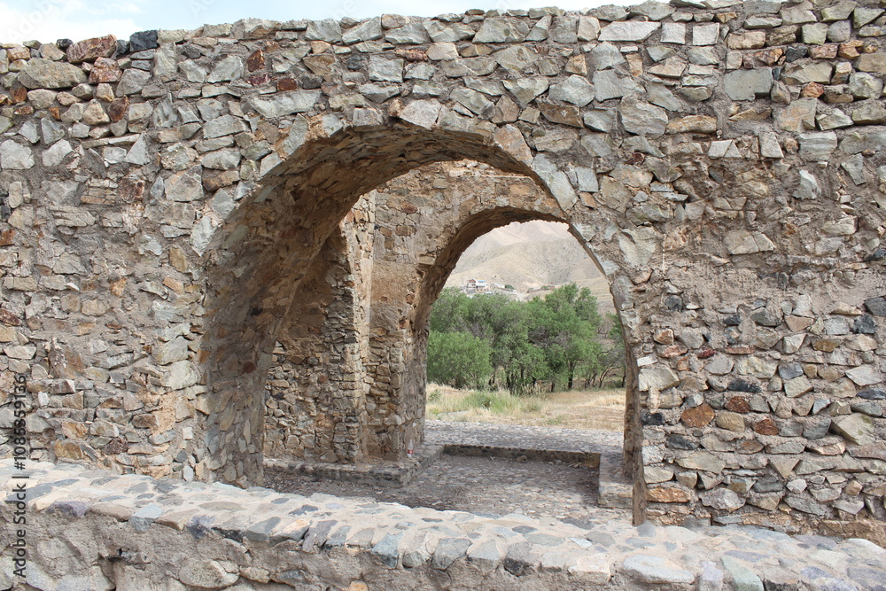 A historical stone archway with open view of the surrounding mountainous landscape and cloudy sky. A historical stone archway with open view of the surrounding mountainous landscape and cloudy sky.