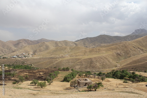 Historical stone structure on dry land with distant mountains under cloudy sky, showcasing ancient heritage. photo